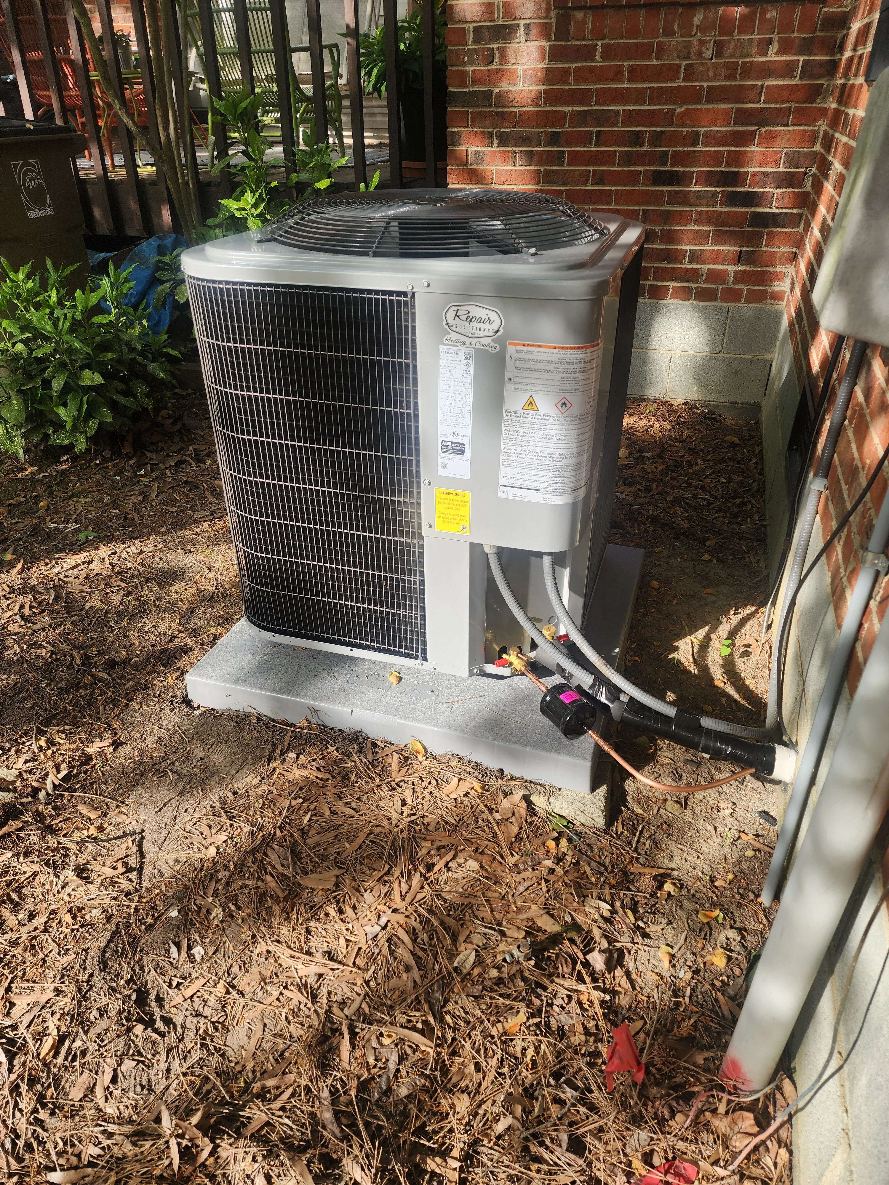 New AC condenser unit installed on concrete pad with refrigerant lines and electrical connections