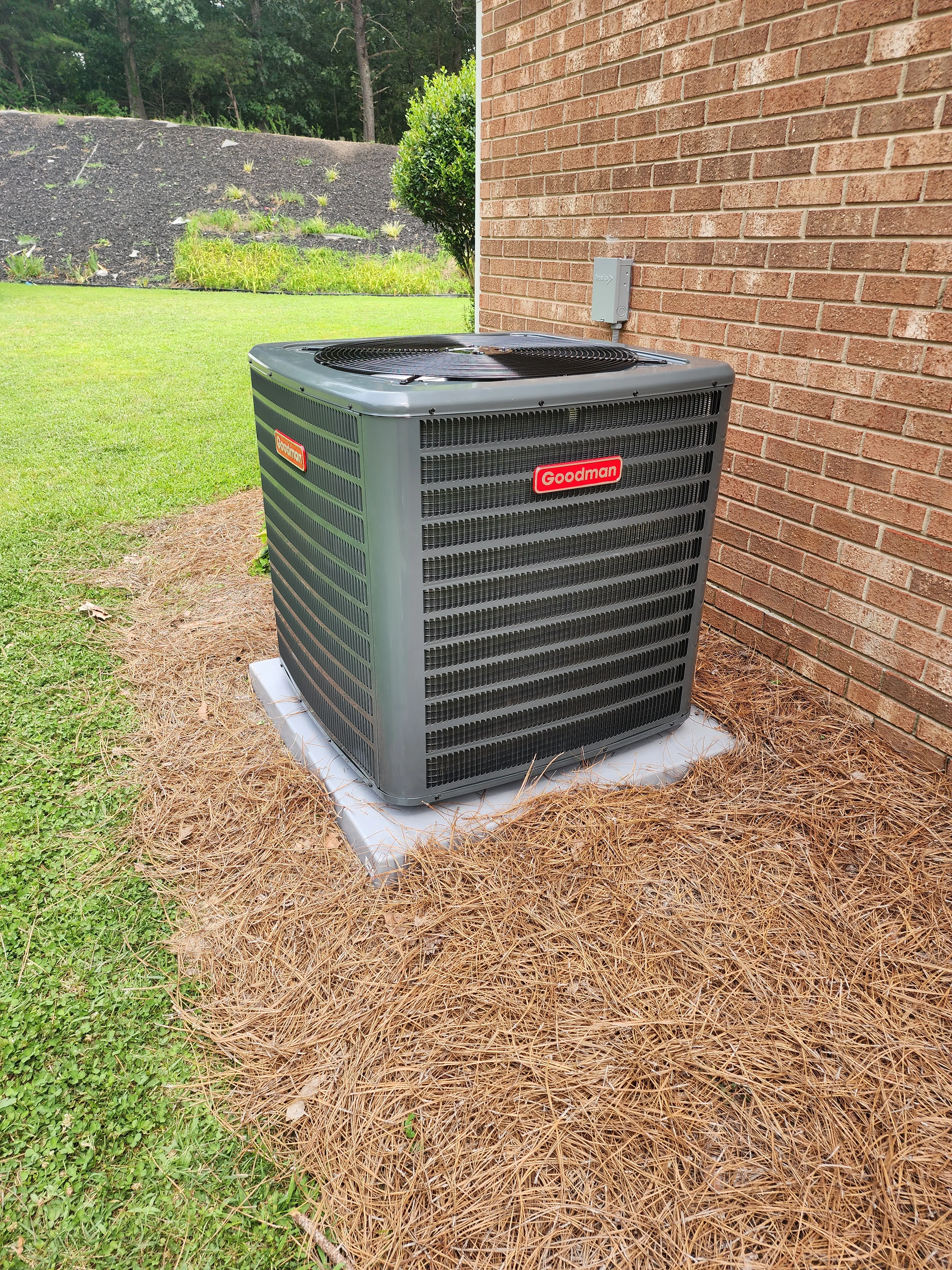 Goodman AC condenser unit installed on concrete pad next to brick home
