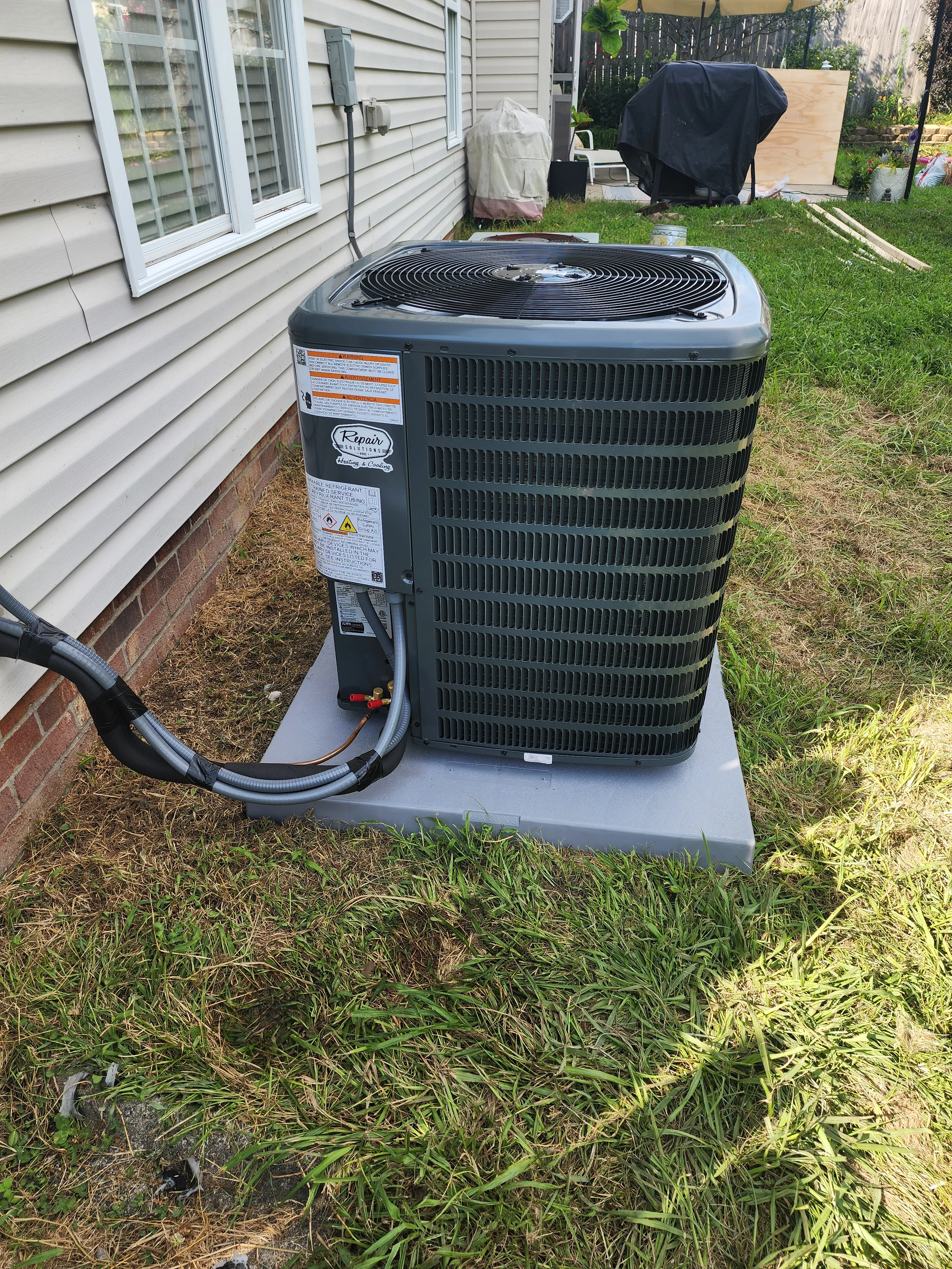 New black air conditioning condenser unit on concrete pad with refrigerant lines connected