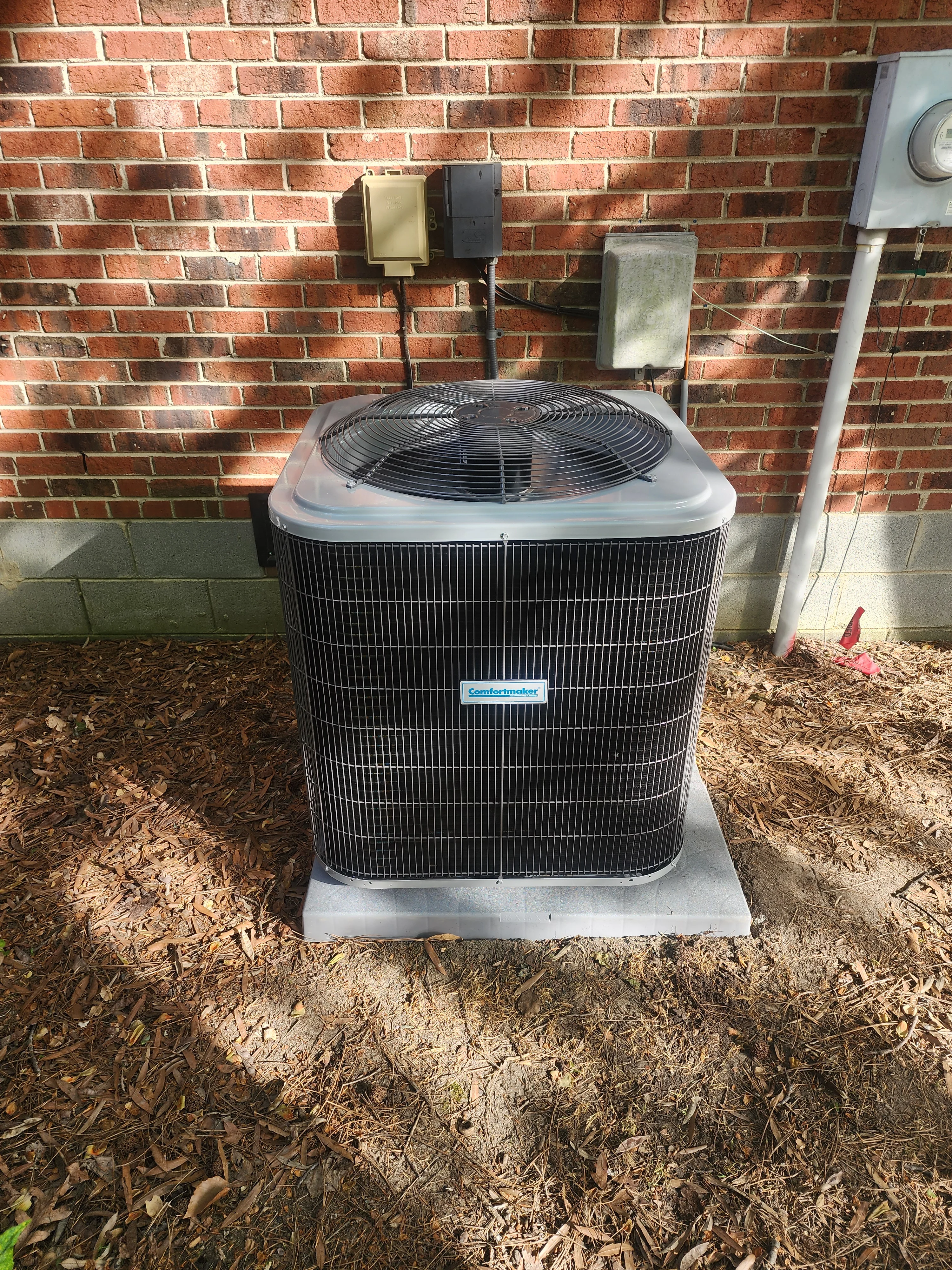 New Comfortmaker AC condenser unit on concrete pad with electrical connections and brick wall mounting