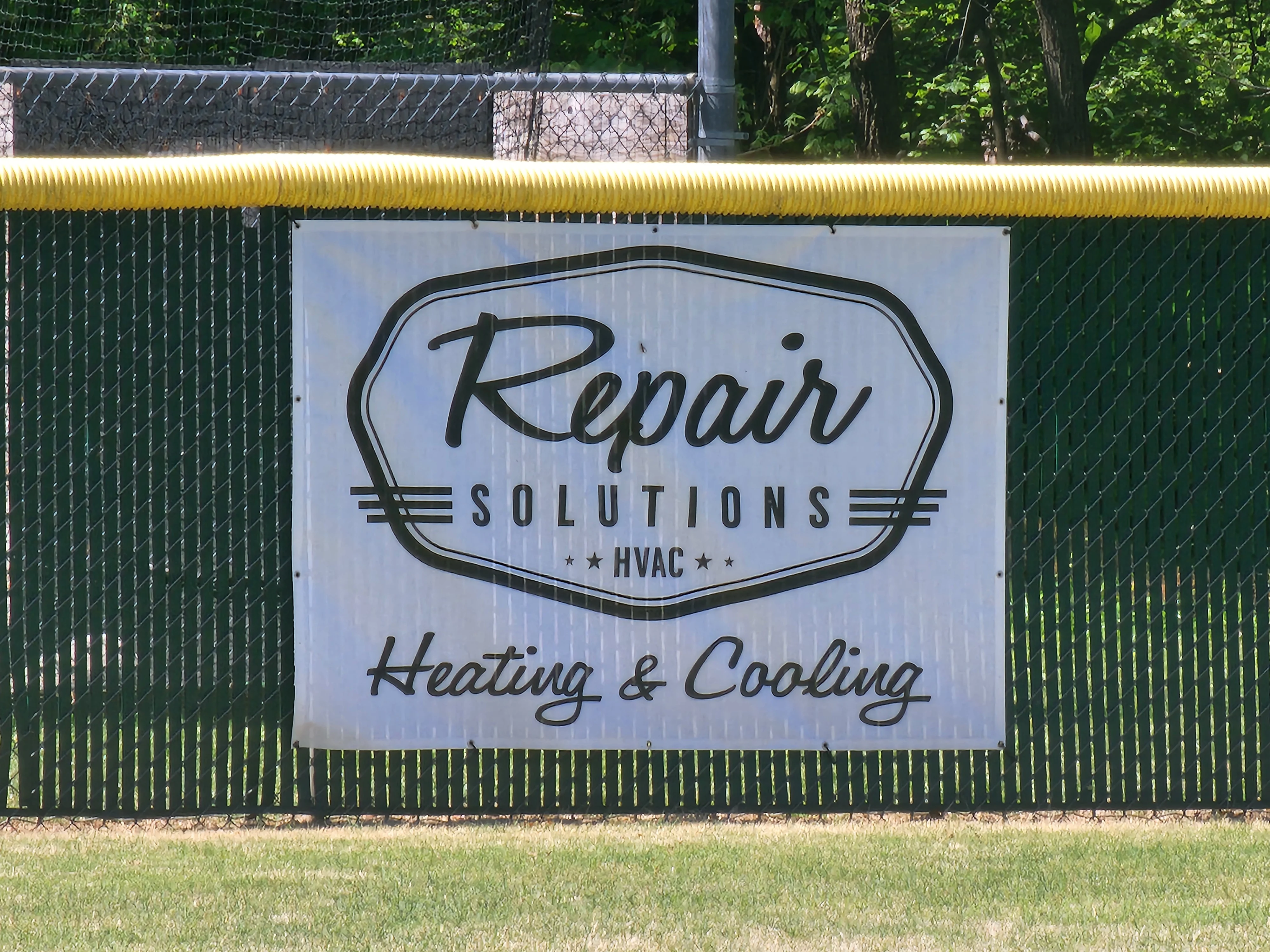 Vinyl banner sign on metal fence with HVAC company branding and heating cooling text