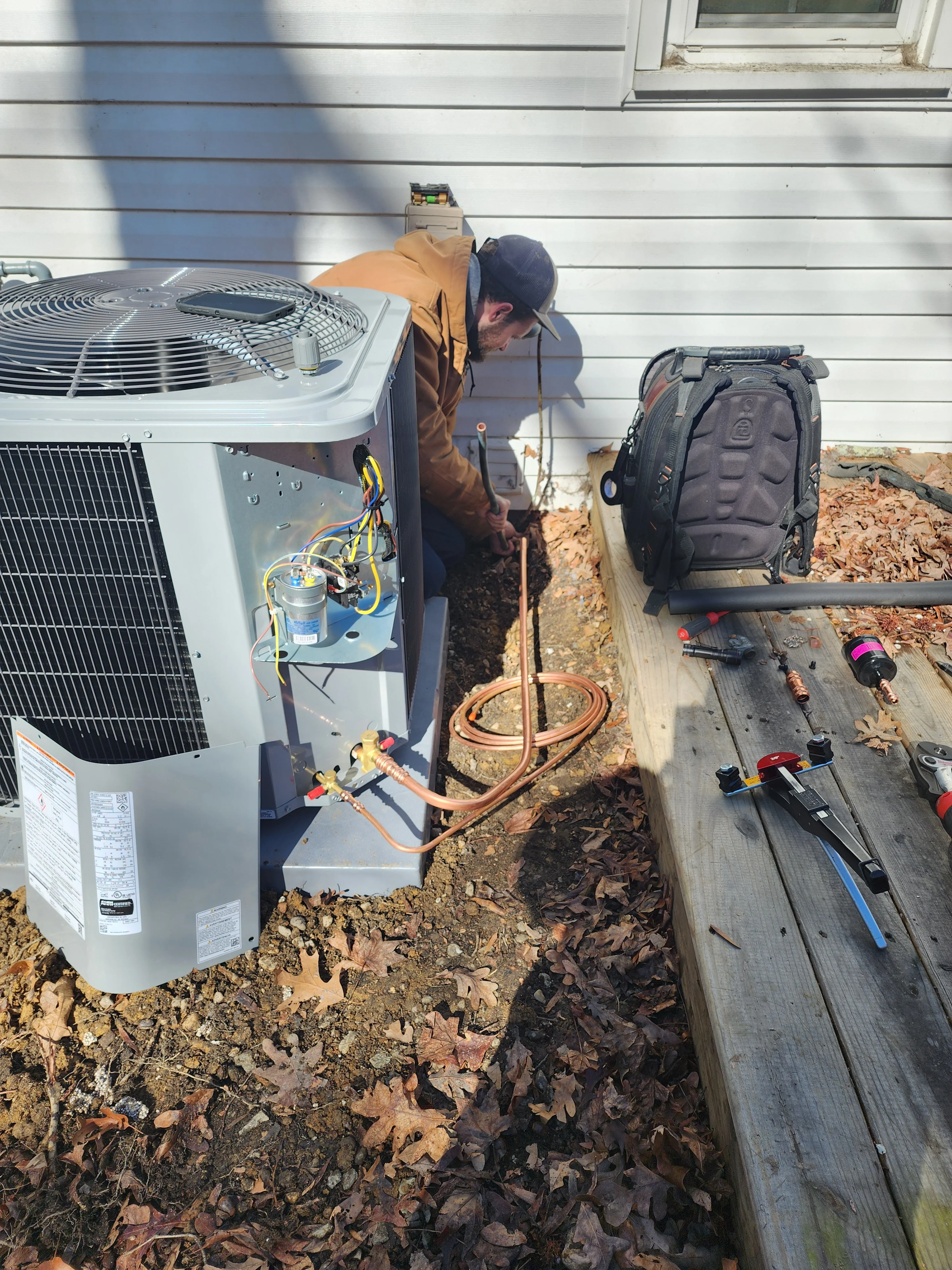 HVAC technician installing heat pump unit with copper refrigerant lines and electrical connections